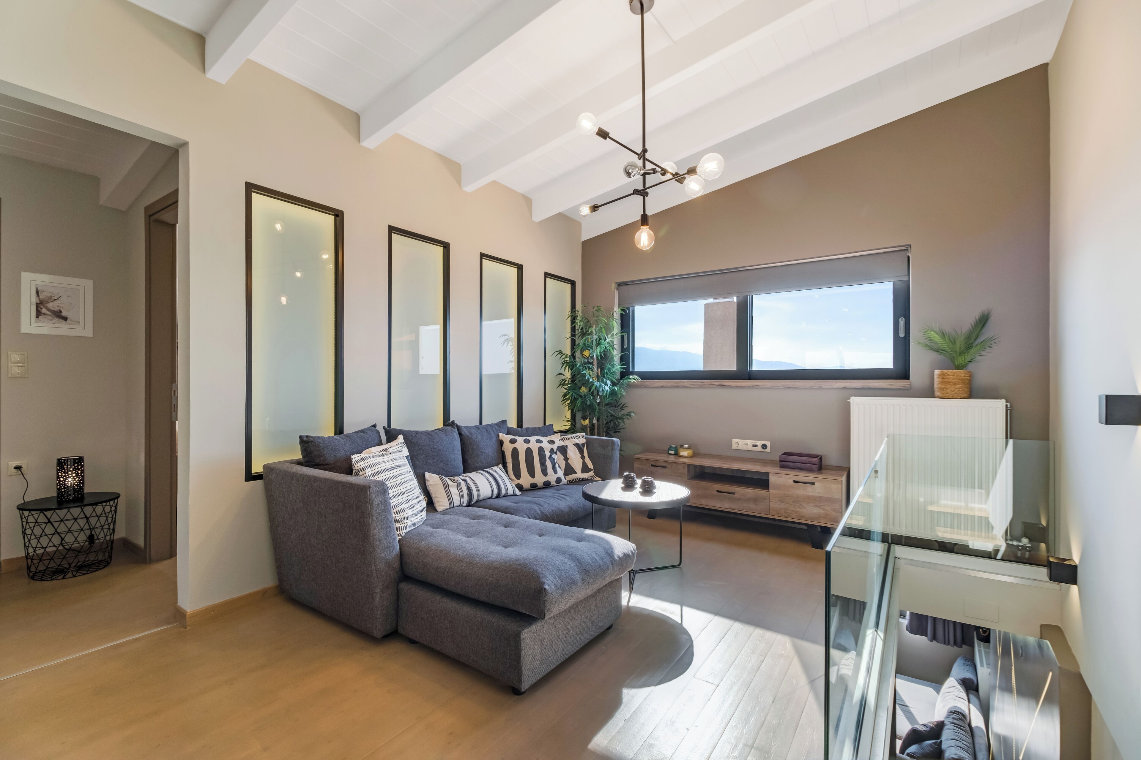 A modern living room with a grey sectional sofa, a glass coffee table, and a large window with a view.