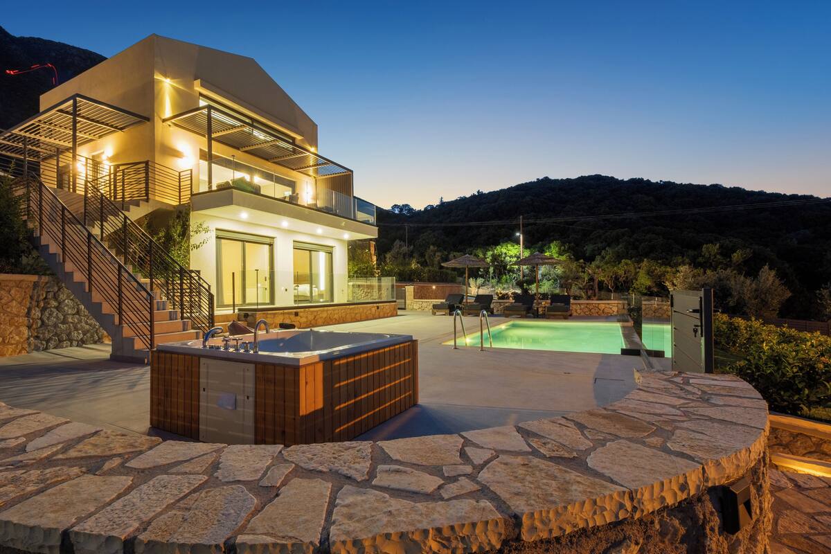 Une maison moderne à deux étages dotée d’une piscine, d’un jacuzzi extérieur et d’une terrasse en pierre.