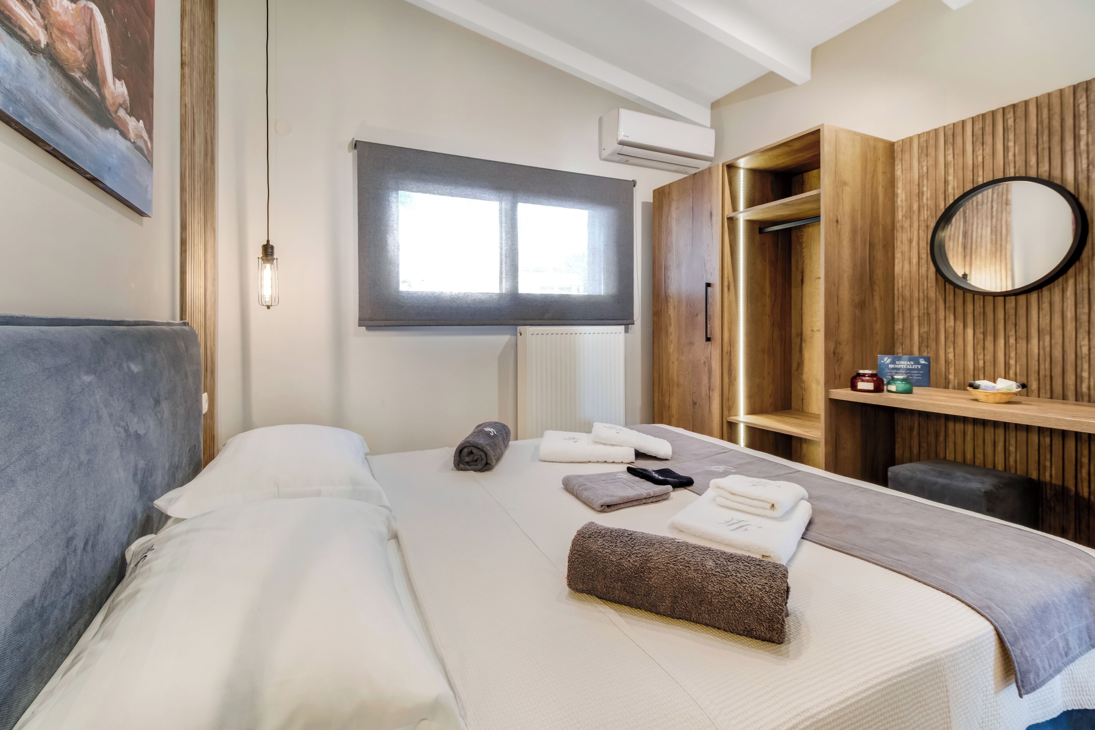 Ein Hotelzimmer mit Bett, Fenster, Klimaanlage, Spiegel und Ablagefläche mit Toilettenartikeln.
