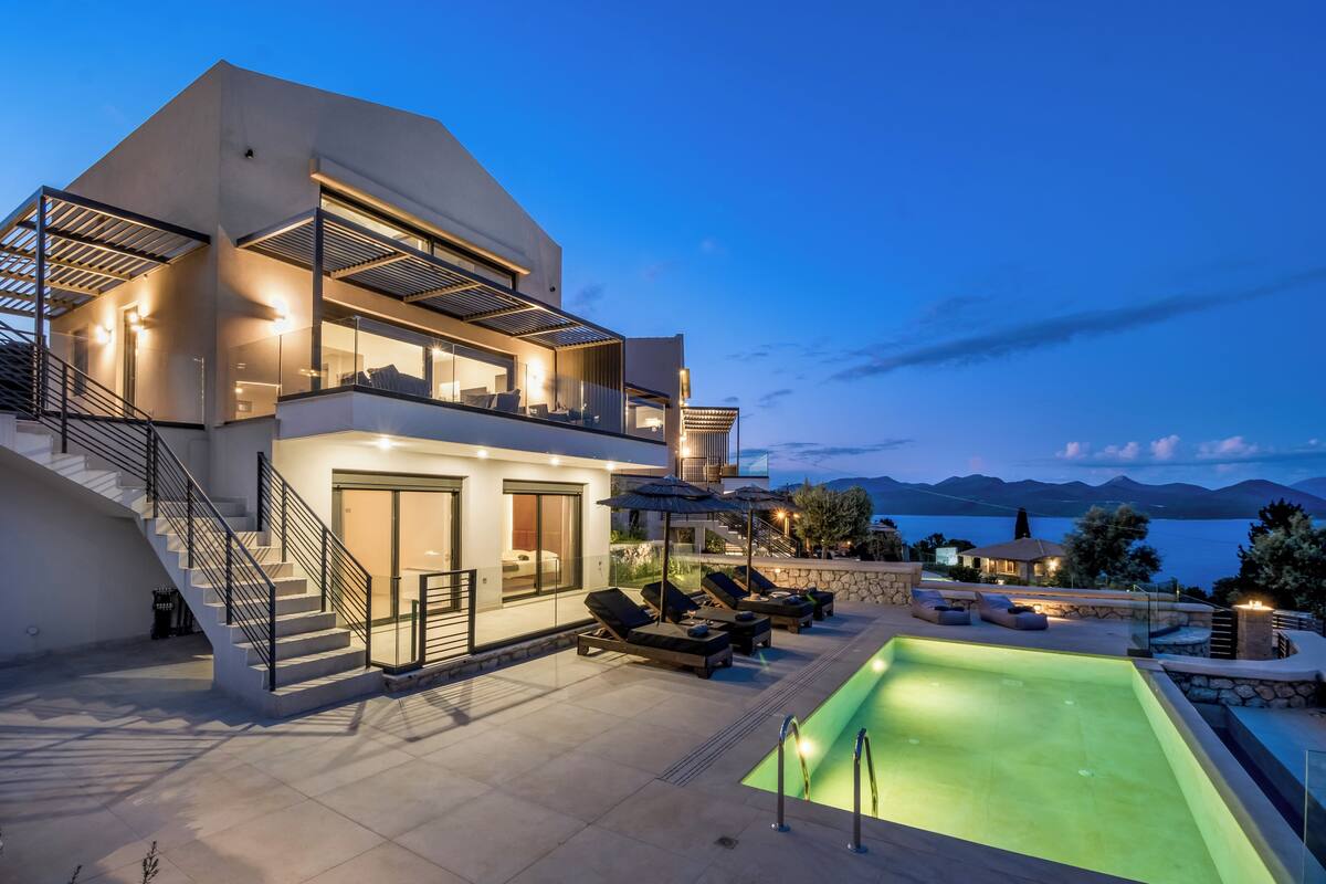 Une maison moderne à deux étages, dotée d’une piscine, d’un espace salon extérieur et offrant une vue sur les montagnes.