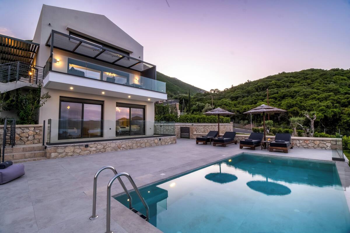 Une maison moderne à deux étages, dotée d’une piscine, d’un espace salon extérieur et offrant une vue sur une colline verdoyante.