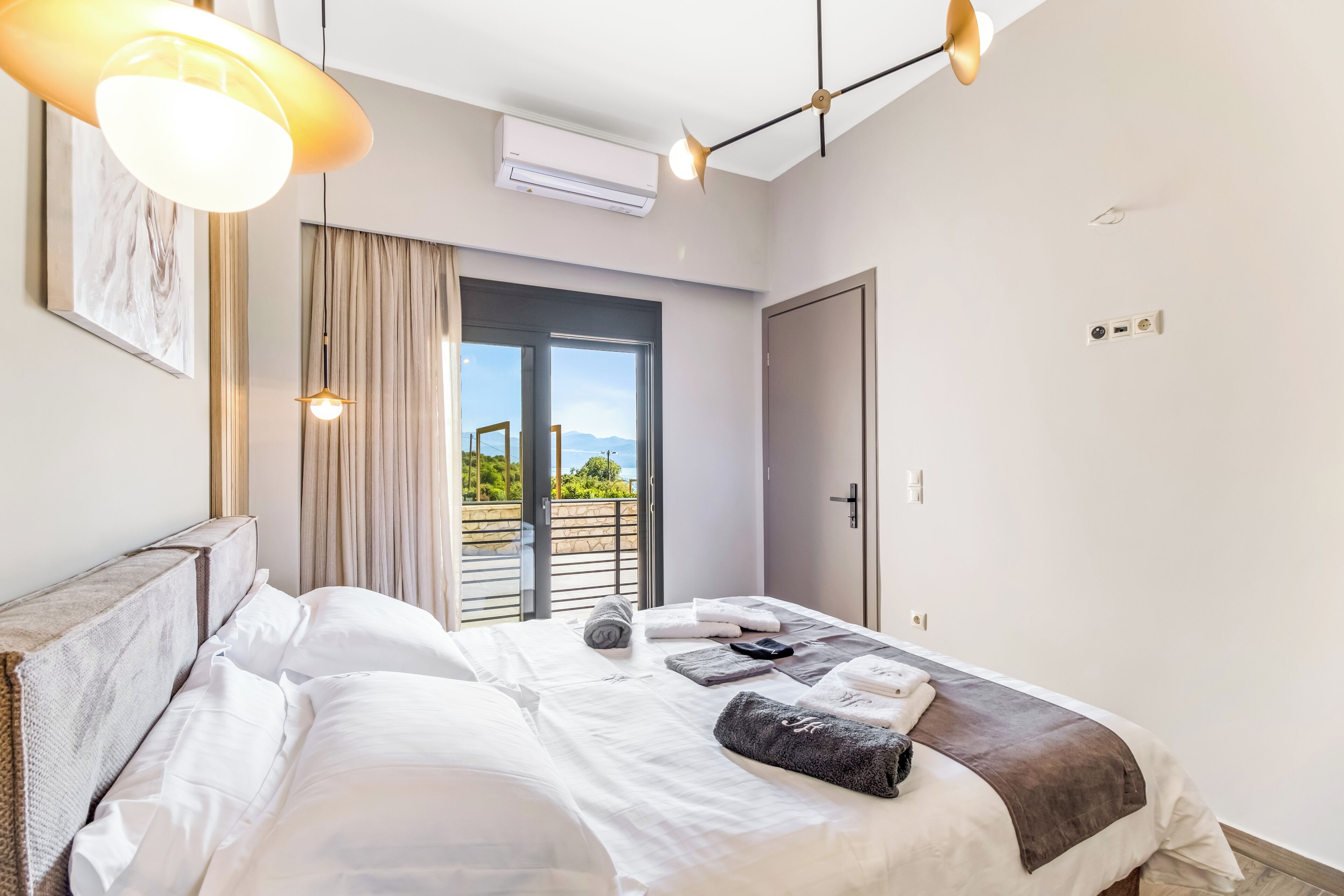 A modern hotel room with a bed, a large window, an air conditioning unit, and a door.