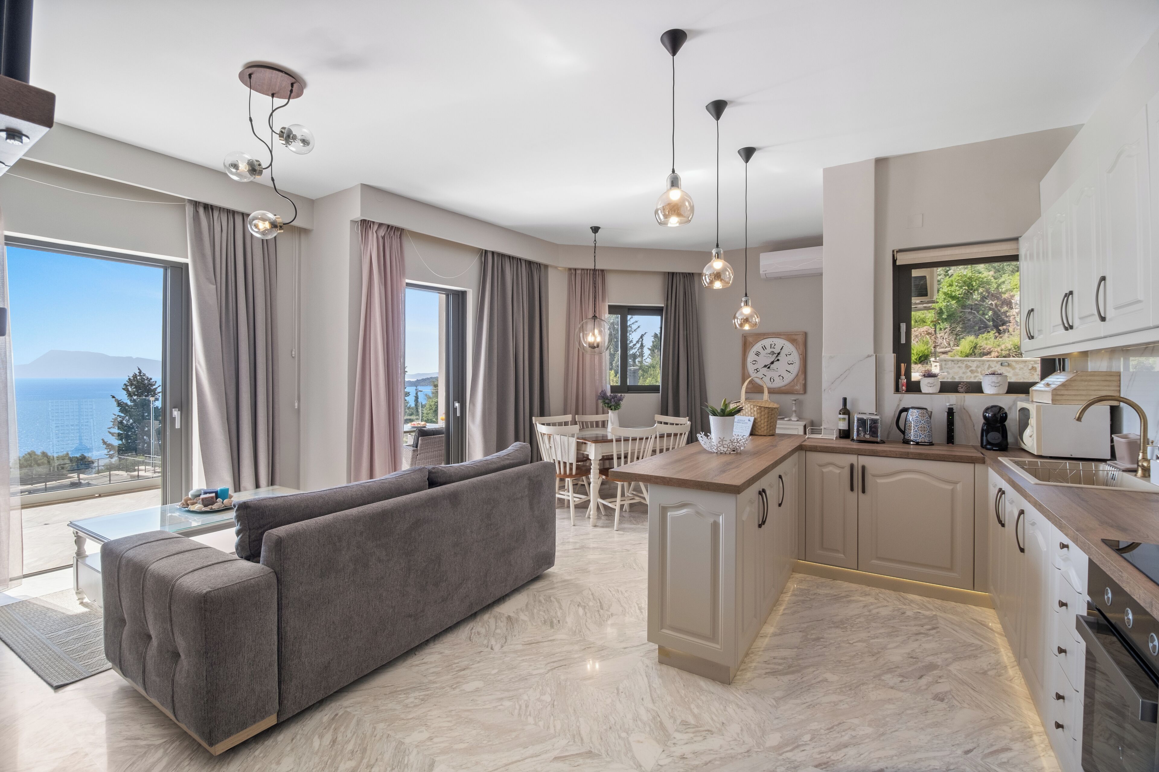 A modern kitchen with a dining area, a sofa, and a view of the sea.