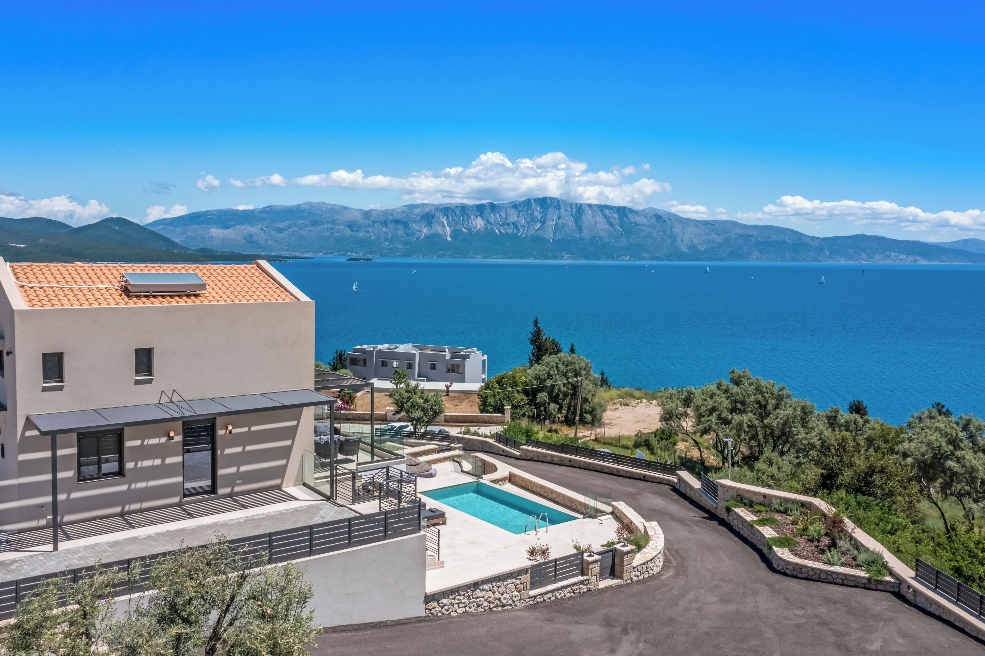 A modern villa with a swimming pool, a covered patio, and a view of the sea and mountains.