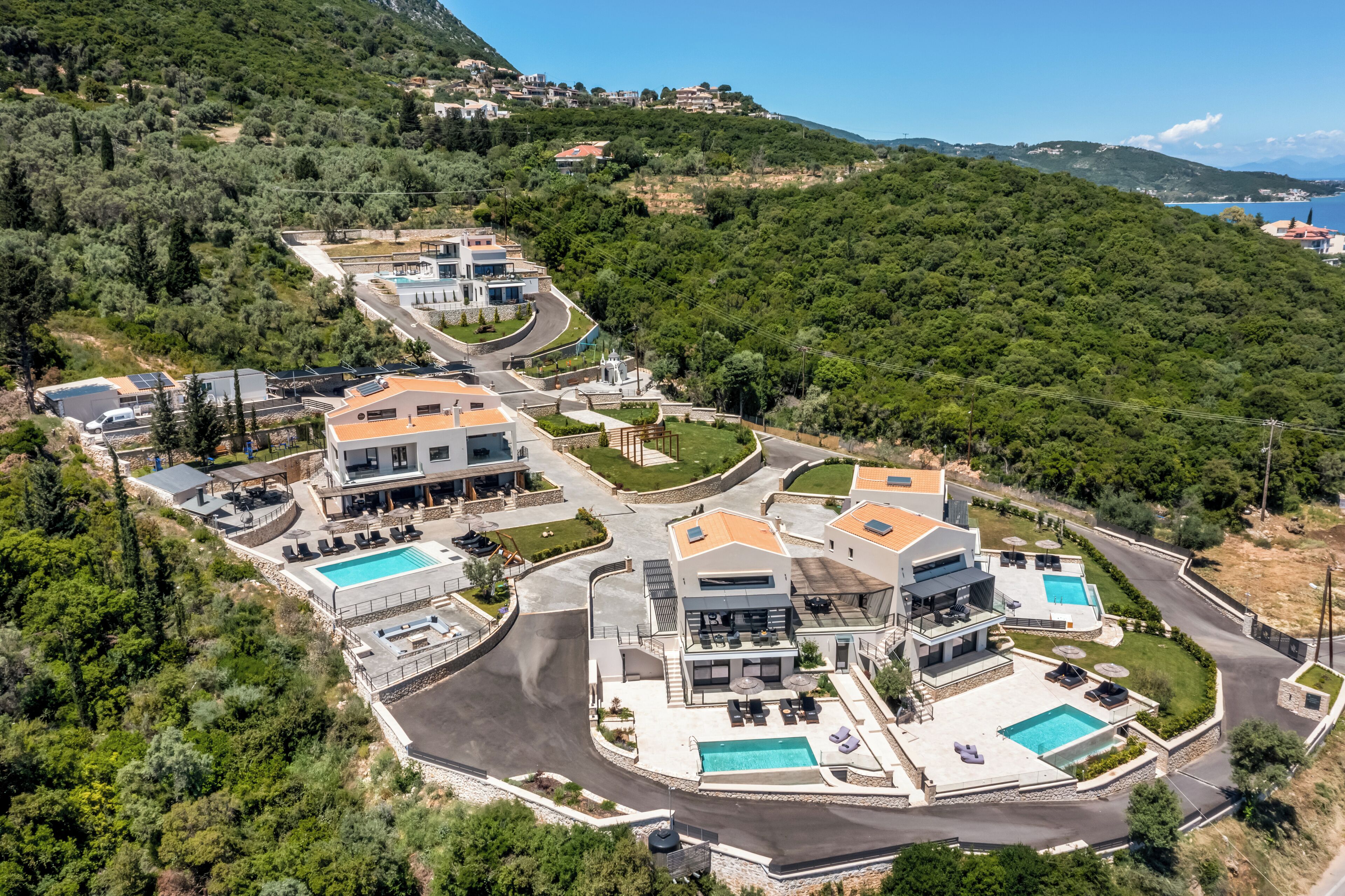A modern residential complex with multiple houses, a central pool area, and a hilly backdrop.