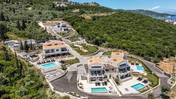 A modern residential complex with multiple houses, a central pool area, and a hilly backdrop.