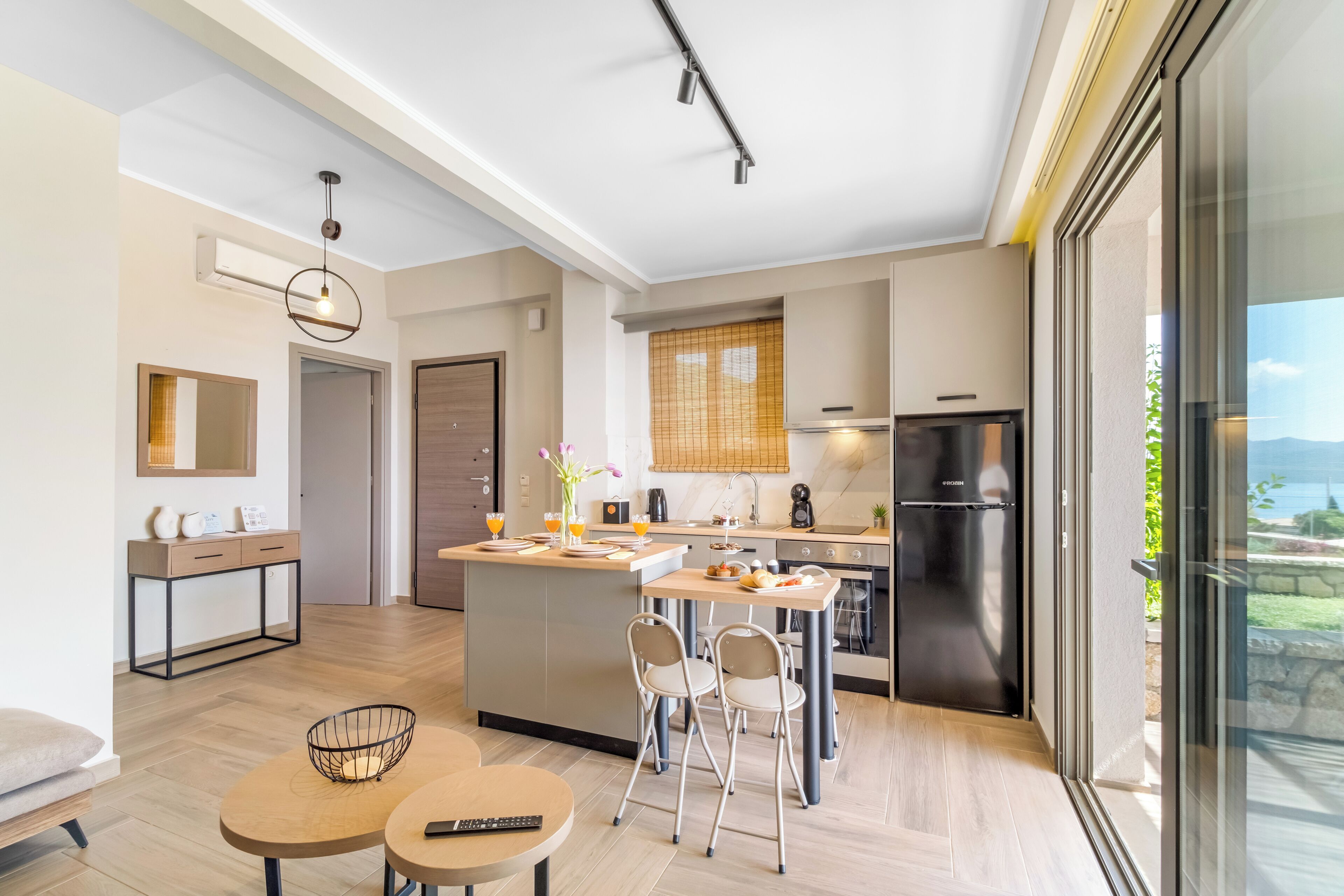 A modern kitchen with a central island, a dining area with chairs, and a large sliding glass door to the outdoors.