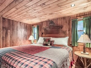 Quarto com painéis de madeira, uma cama, duas luminárias de cabeceira e uma janela com cortinas.
