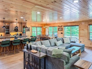A spacious cabin interior with a large wooden ceiling, a dining area, a seating area with a sofa, and a bar with stools.