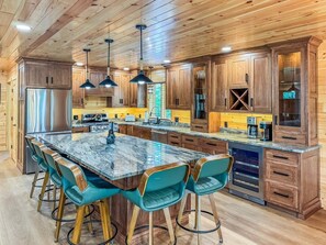 A modern kitchen with wooden cabinets, a marble island, and teal bar stools.