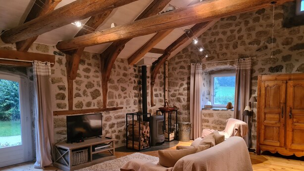 A cozy room with stone walls, wooden beams, a fireplace, a television, and a large window. - La ferme des Farios 4 pers (Tence)