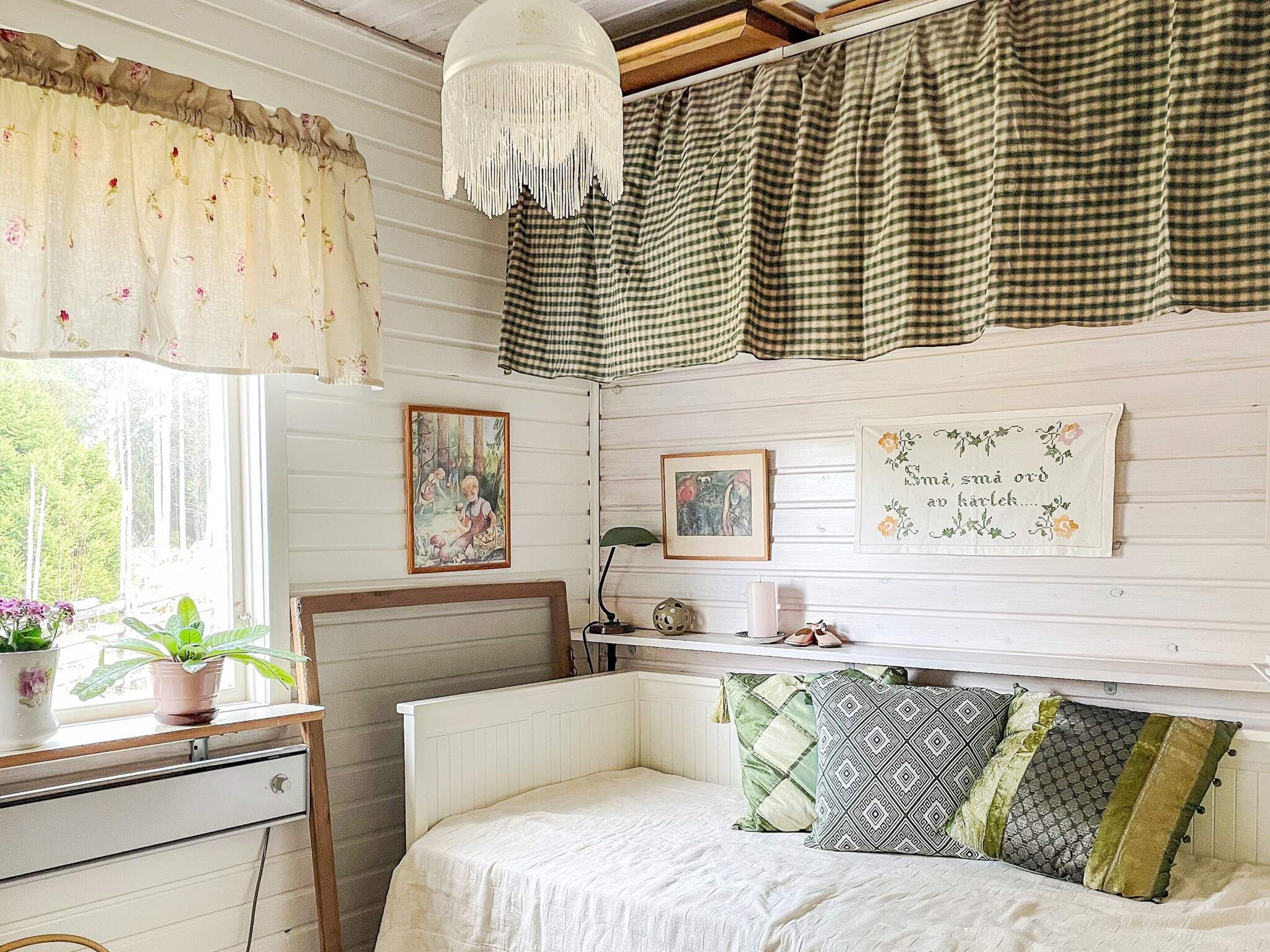 Ein Schlafzimmer mit Bett, Kommode, Fenster mit Vorhängen und Wanddekorationen.