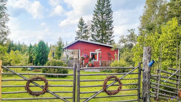A red barn with a porch, surrounded by a wooden fence with wreaths. - 5 Person Holiday Home in Hallstavik (Hallstavik)