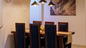 Un espace repas comprenant une table et des chaises en bois, des luminaires suspendus et un ventilateur fixé au mur.