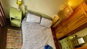 Une chambre avec un lit, une table de chevet, une commode, un radiateur et un tableau.