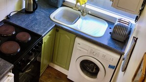 Une cuisine de taille réduite, équipée d’une cuisinière, d’un évier et d’un lave-linge.