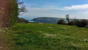 Un champ verdoyant offrant une vue dégagée sur la côte et sur des collines lointaines.