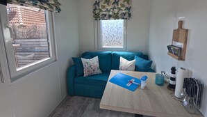 A compact living space with a teal sofa, a small table with a blue folder, and a window with a patterned valance. - Crab on the Rhön beach with whirlpool (Wartmannsroth)