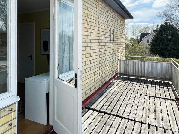 Eine Holzterrasse mit Metallgeländer, eine Tür zu einem Raum und eine Backsteinmauer.