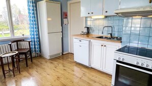 Pieni, käytännöllinen keittiö, jossa on jääkaappi, liesi, pesuallas ja puiset tuolit.