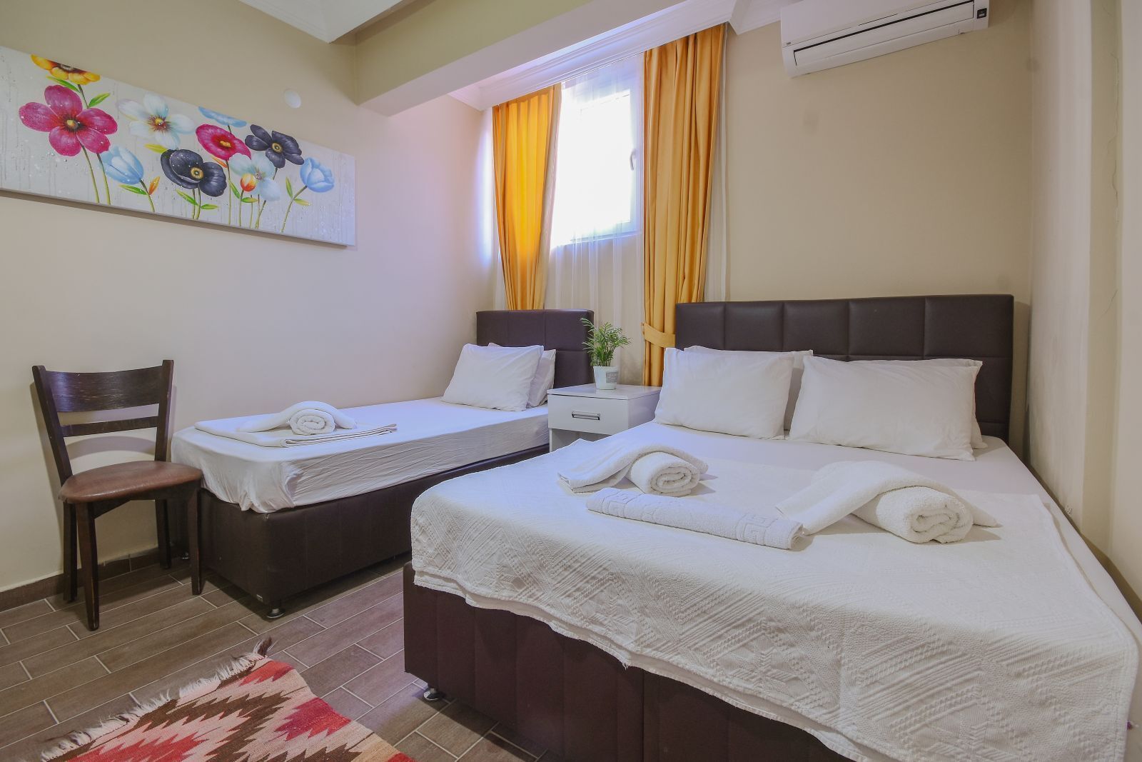 A hotel room with two beds, a chair, a painting on the wall, and a window with curtains.