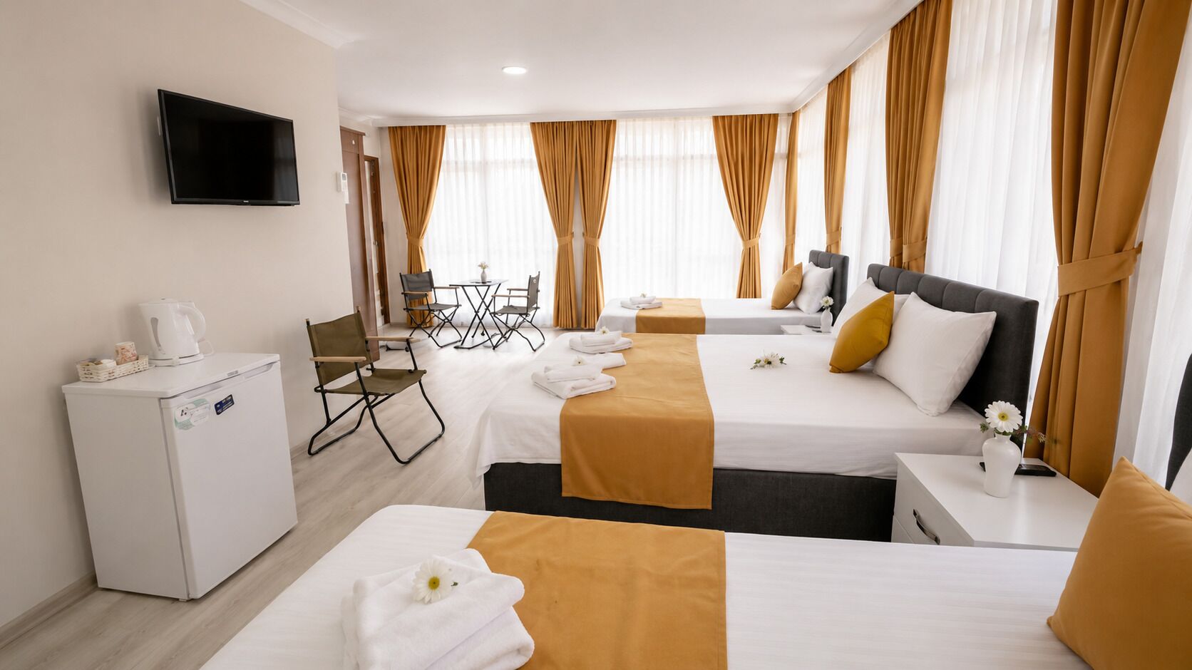 A hotel room with two beds, a TV, a mini-fridge, a dining table with chairs, and a window with curtains.