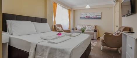 A hotel room with a bed, a sofa, a chair, a TV, and a painting on the wall.