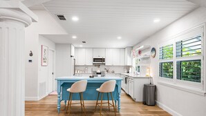 Een moderne keuken met witte kasten, een blauw eiland en twee barkrukken.