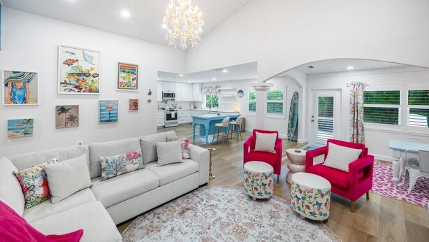 Een ruime woonkamer met een bank, fauteuils en een salontafel. In de achtergrond bevindt zich een keuken met een blauw kookeiland.