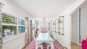 Een eetgedeelte met een blauwe tafel, witte stoelen en een roze vloerkleed met luipaardprint.