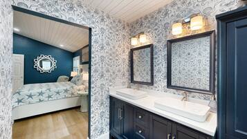 A bedroom with a bed, a large mirror, and a bathroom with a sink and vanity.