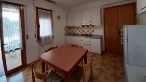 A compact kitchen with a dining table and chairs, a refrigerator, and a window with curtains.