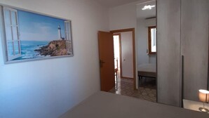 A room with a painting of a lighthouse, a large mirror, and a door leading to another room.