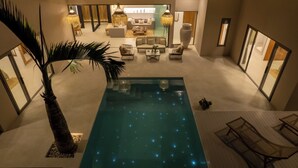 Un espace piscine intérieur moderne, doté d’une piscine à eau claire, de chaises longues et d’un coin salon avec des canapés et une table basse.
