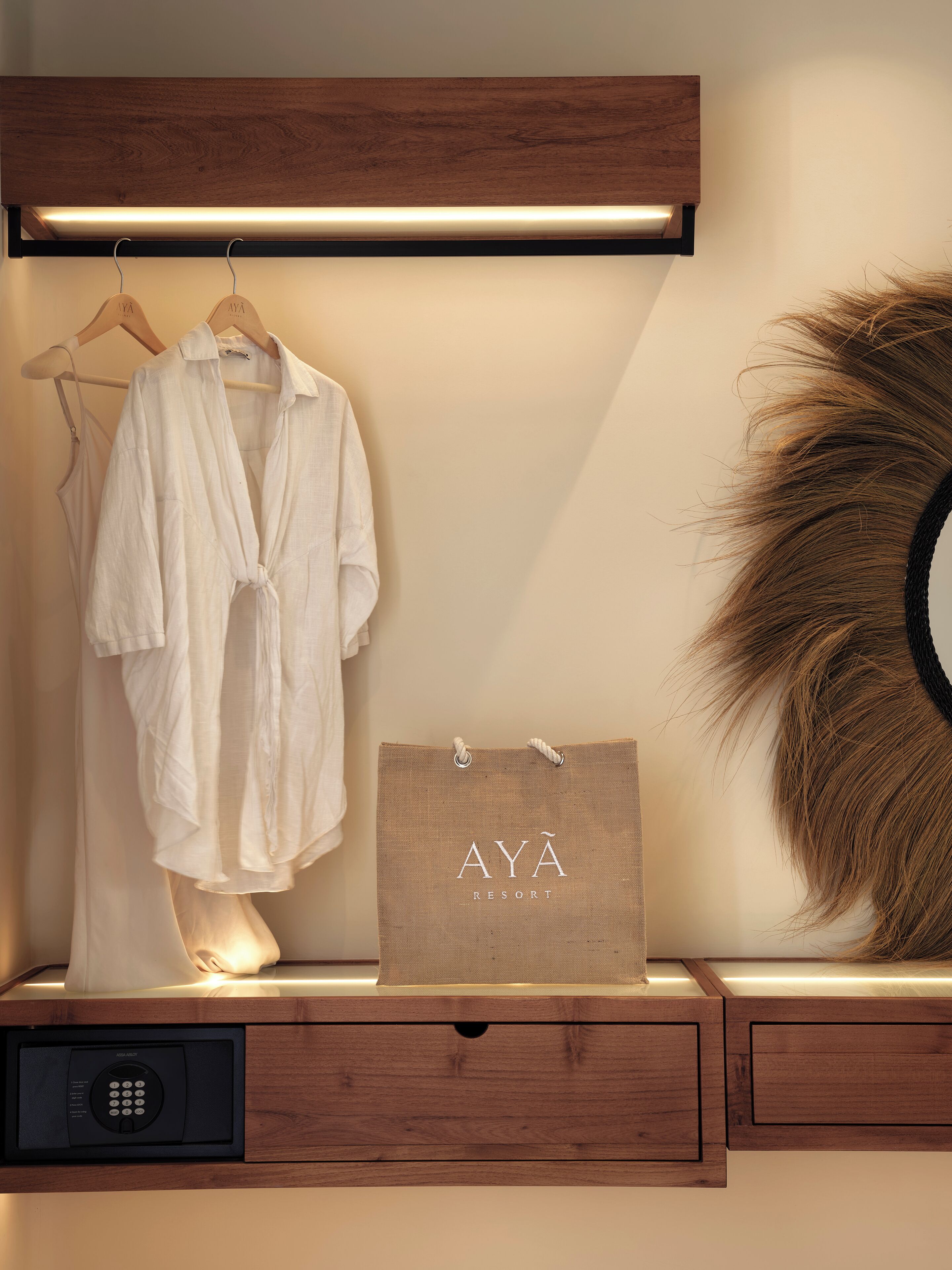 A wooden vanity with a robe, a towel, a mirror, and a bag with 'AYA RESORT' text.