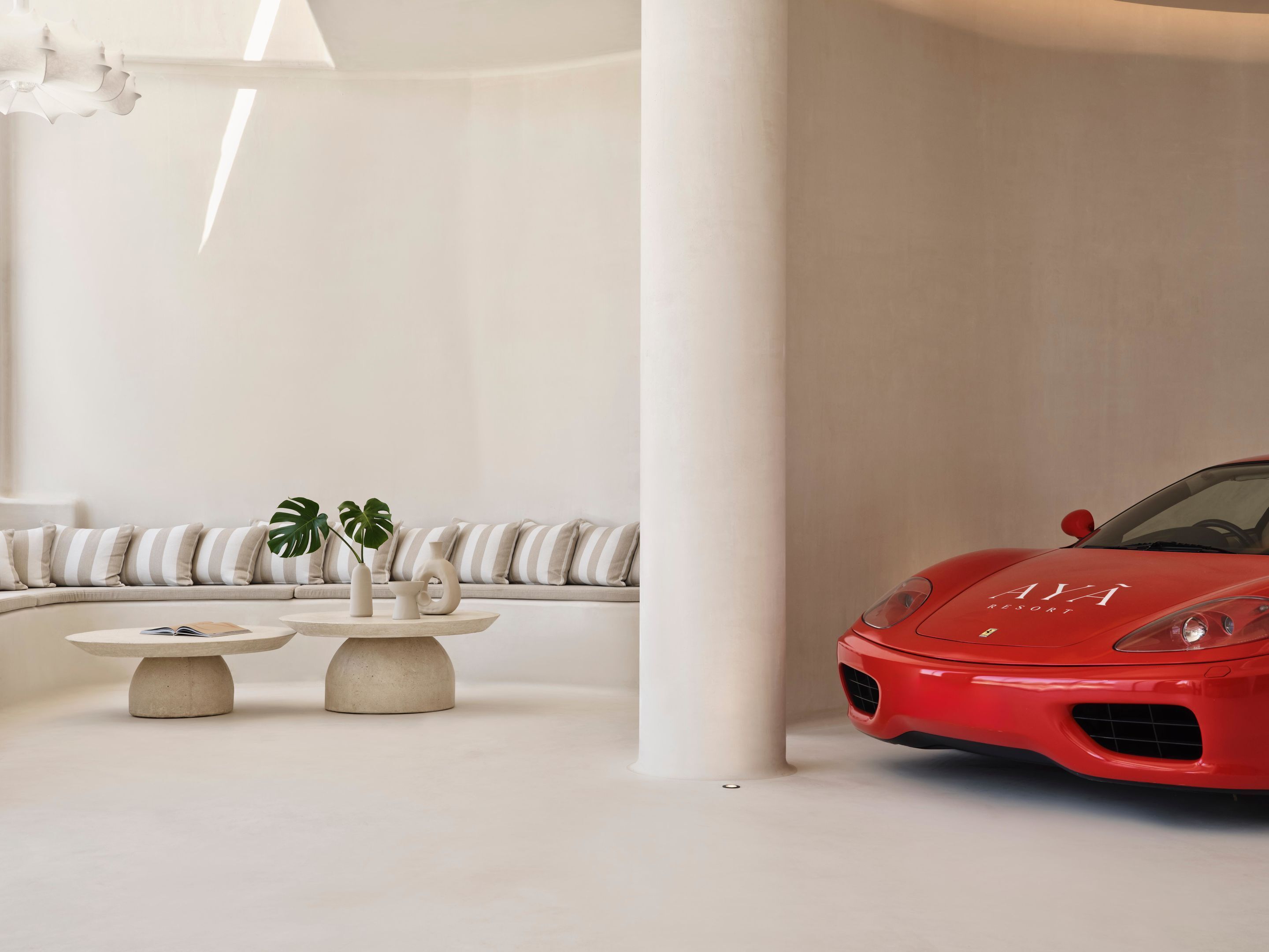A modern interior with a red sports car, a white sofa, and a round table with decorative items.