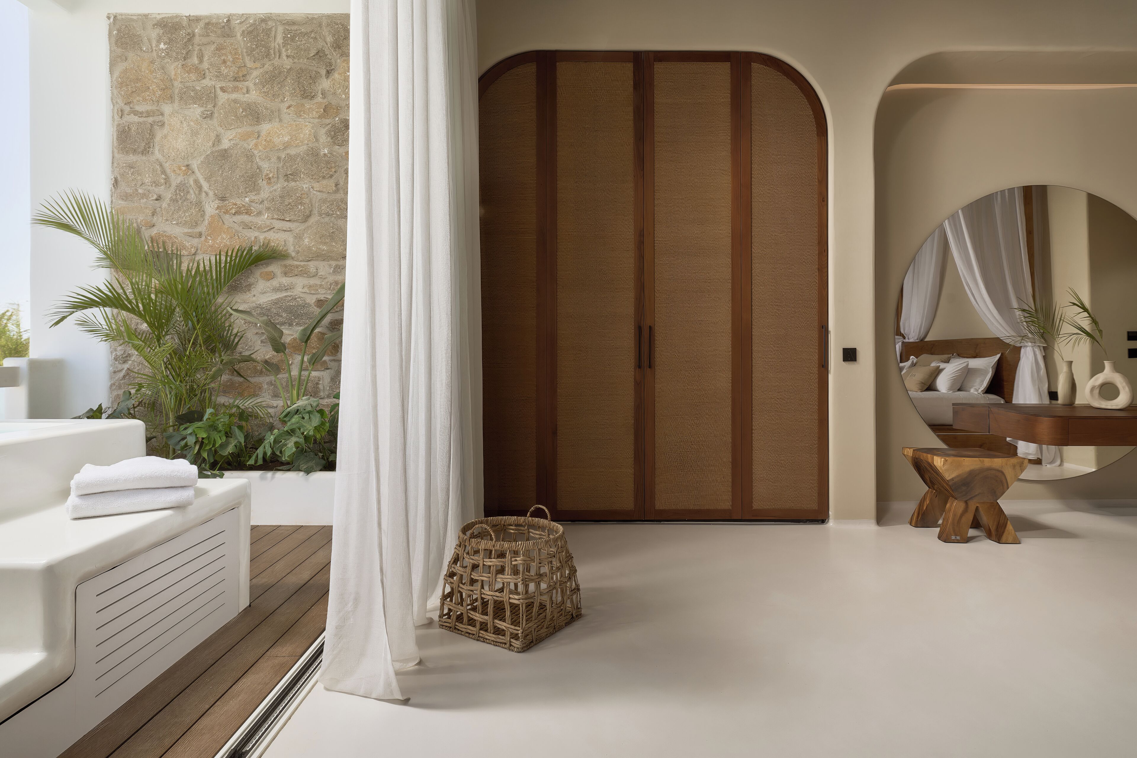 A modern bathroom with a stone wall, a wooden door, a white sink, and a round mirror.
