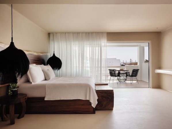 A modern bedroom with a large bed, a hanging light fixture, and a view of an outdoor balcony with chairs. - Aya Resort (Ayia Napa)