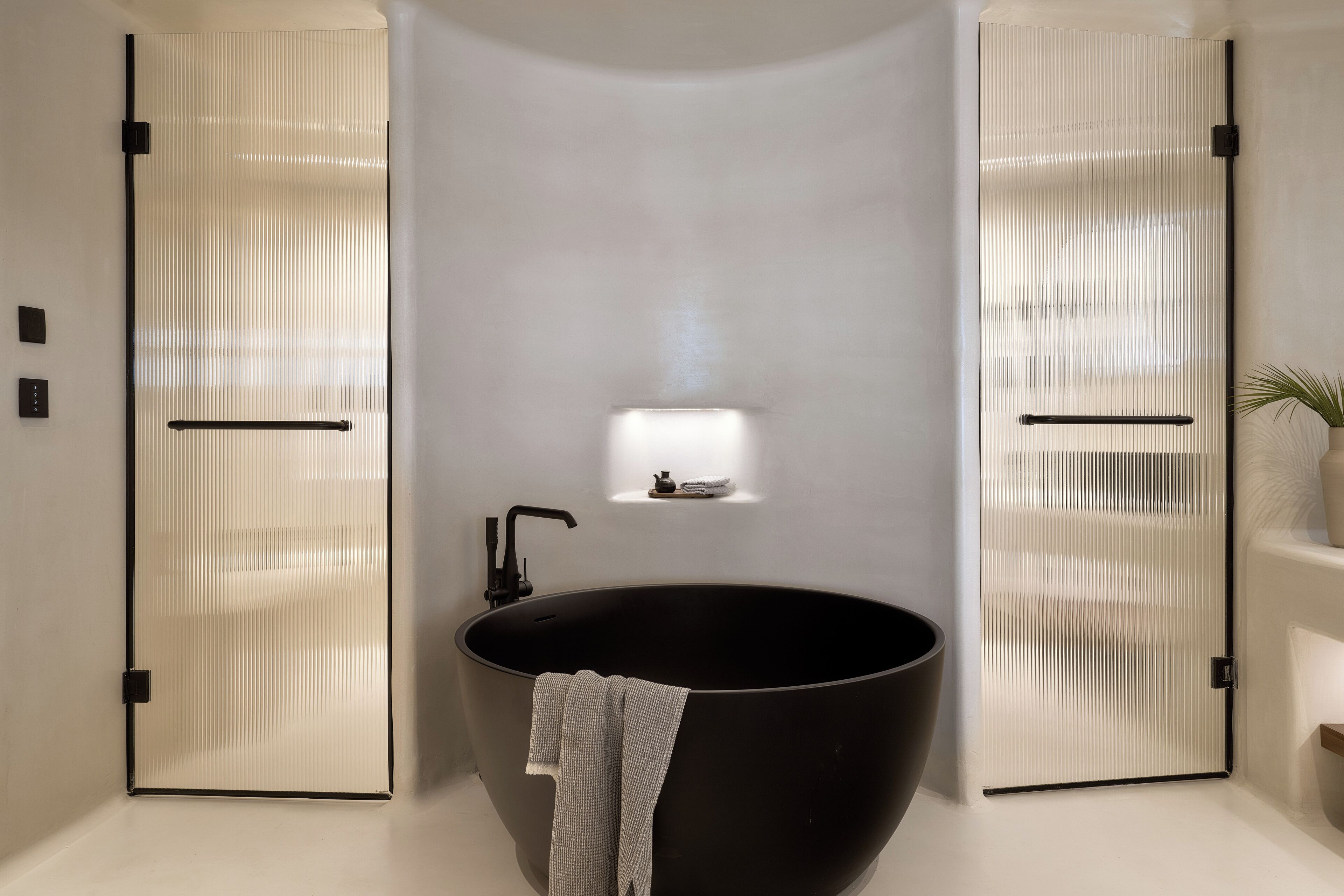 Un baño moderno con un lavamanos negro tipo recipiente, un pequeño estante con luz y dos puertas correderas con persianas verticales.