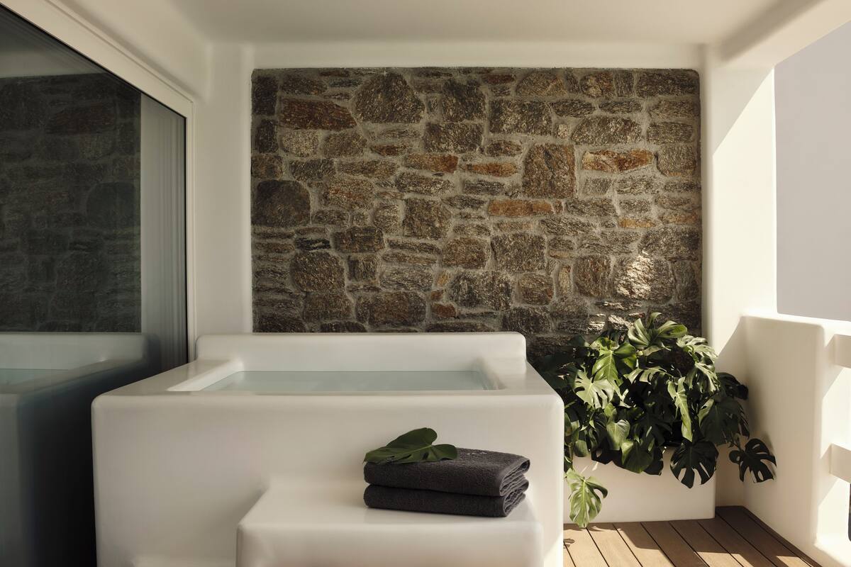 A modern bathroom with a stone wall, a bathtub, and a potted plant.