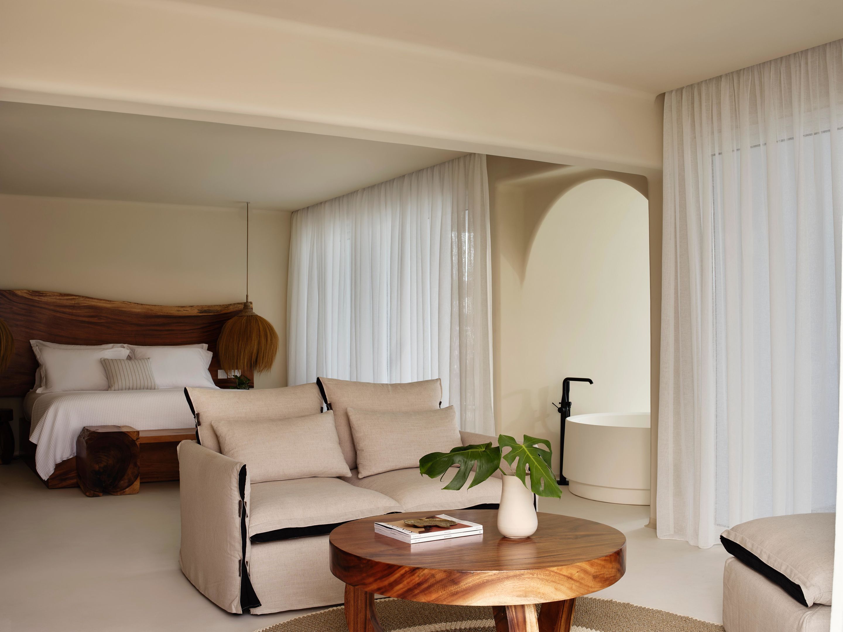 Una habitación de hotel moderna con cama, sofá, una mesa redonda de madera y una planta en maceta.