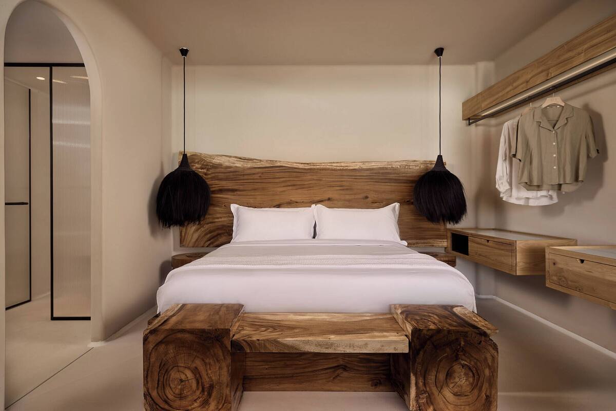 A bedroom with a large bed, wooden headboard, hanging lamps, and a wooden bench.