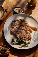 Un plato con bistec a la parrilla, verduras y un recipiente pequeño con salsa.