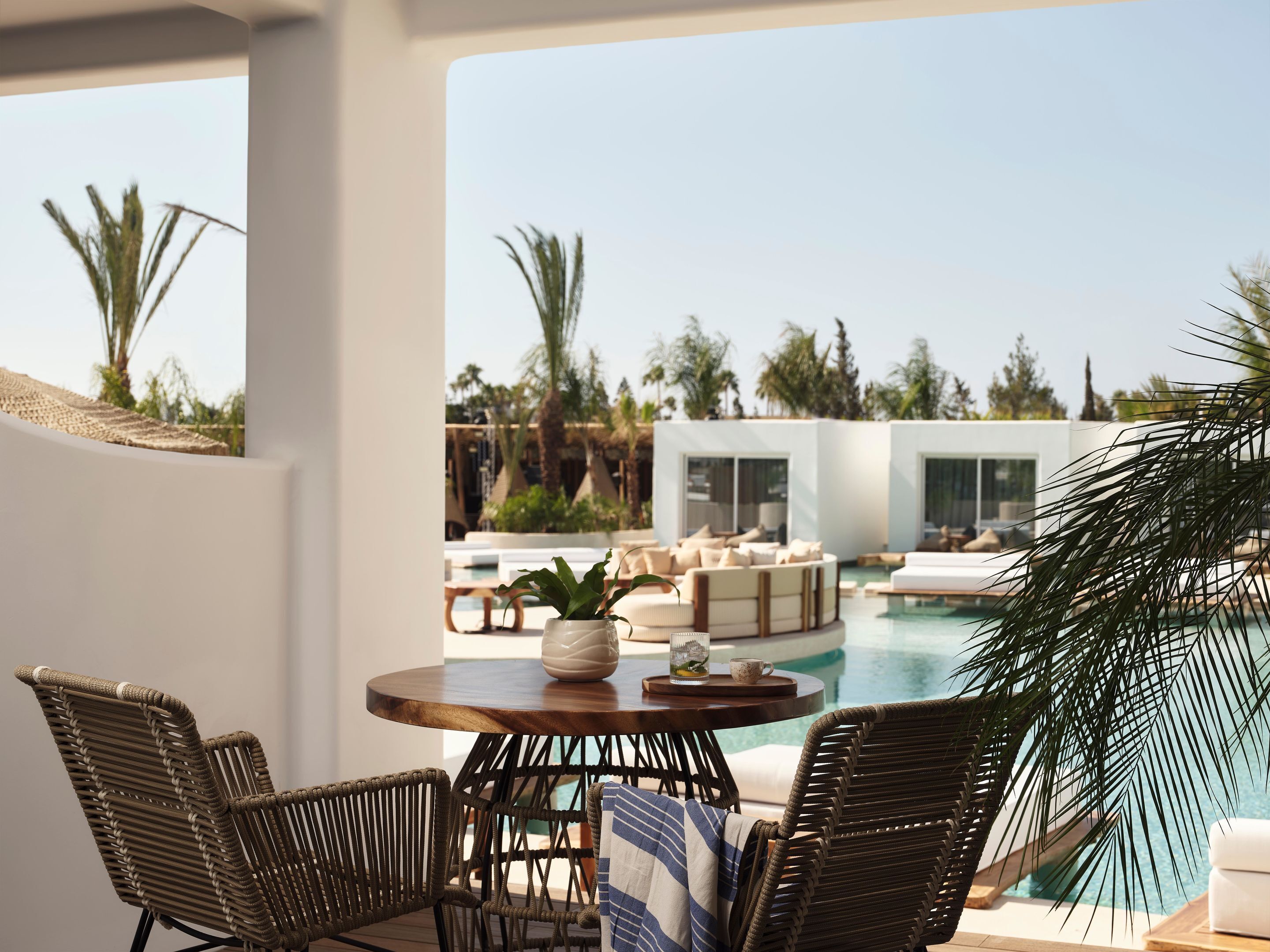 Een zwembadterras met rieten stoelen, een ronde tafel en uitzicht op een modern zwembad en loungegebied.