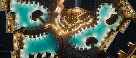 A rooftop pool area with multiple swimming pools, sun loungers, and a central seating area.