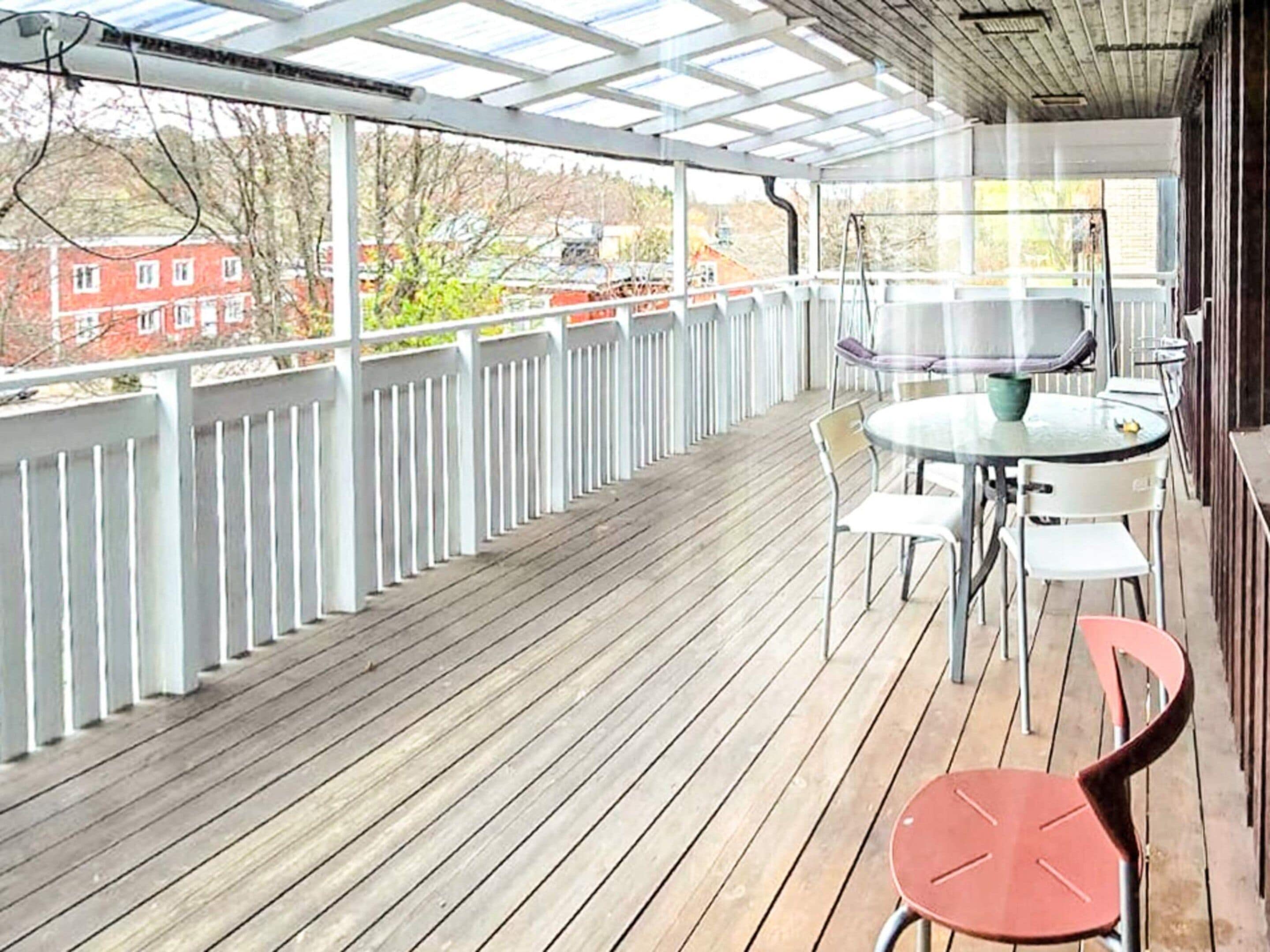 Un espacio al aire libre techado con piso de madera, barandilla blanca y una mesa con sillas.