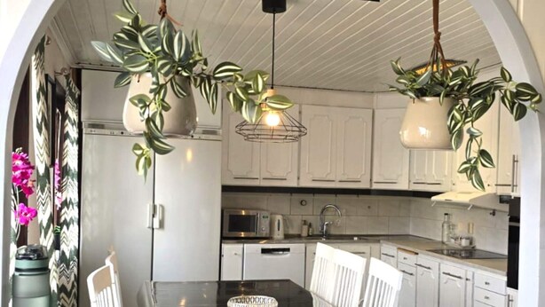 A kitchen with white cabinets, a black countertop, and hanging plants. A 'WELCOME' sign hangs from the ceiling. - 4 Star Holiday Home in Ljusne (Ljusne)