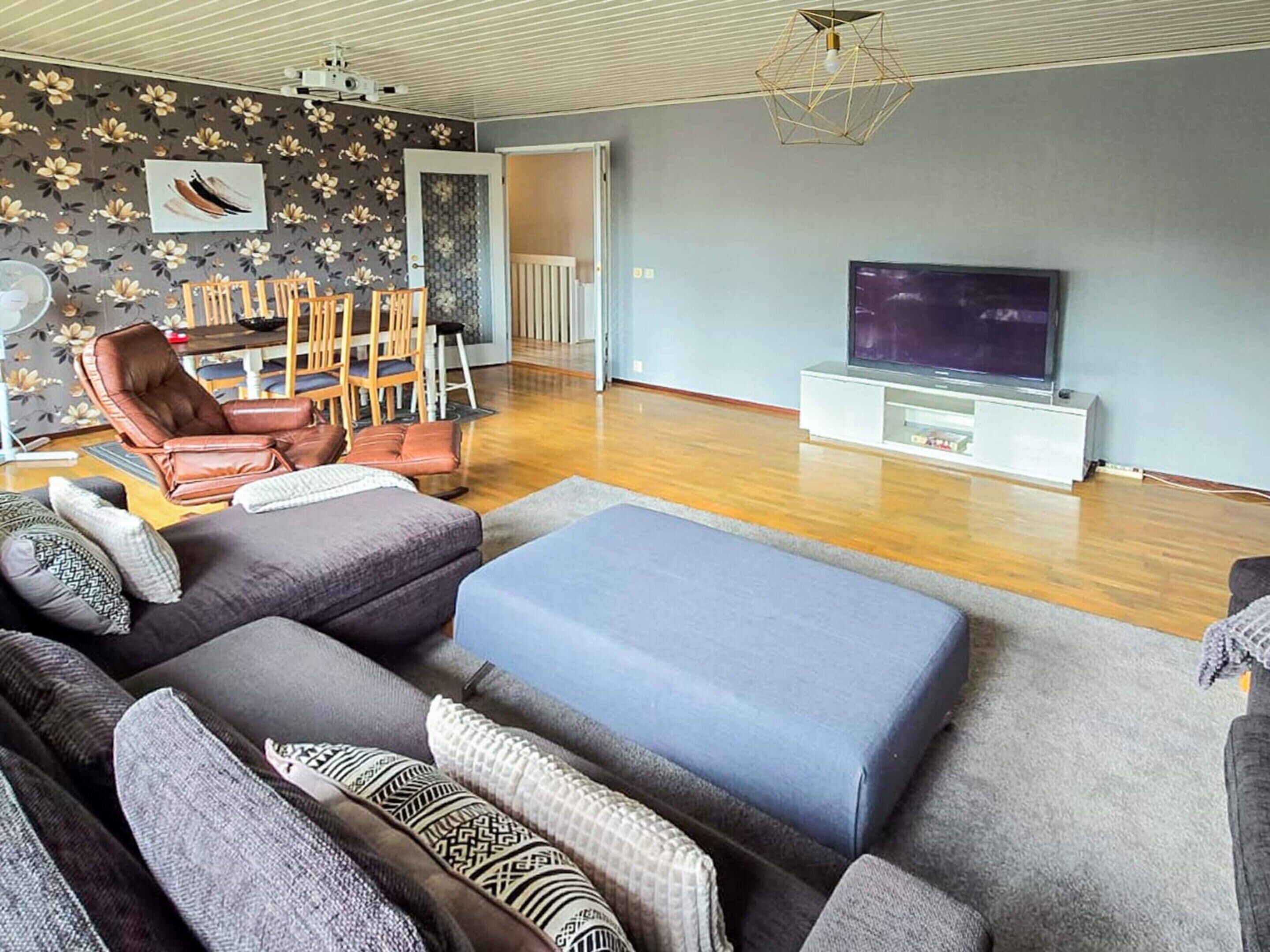 A living room with a sofa, chairs, a TV, and a patterned wall.