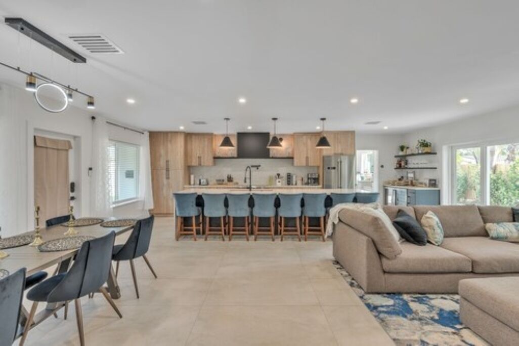A modern kitchen with a central island, bar stools, and a dining area with a table and chairs.