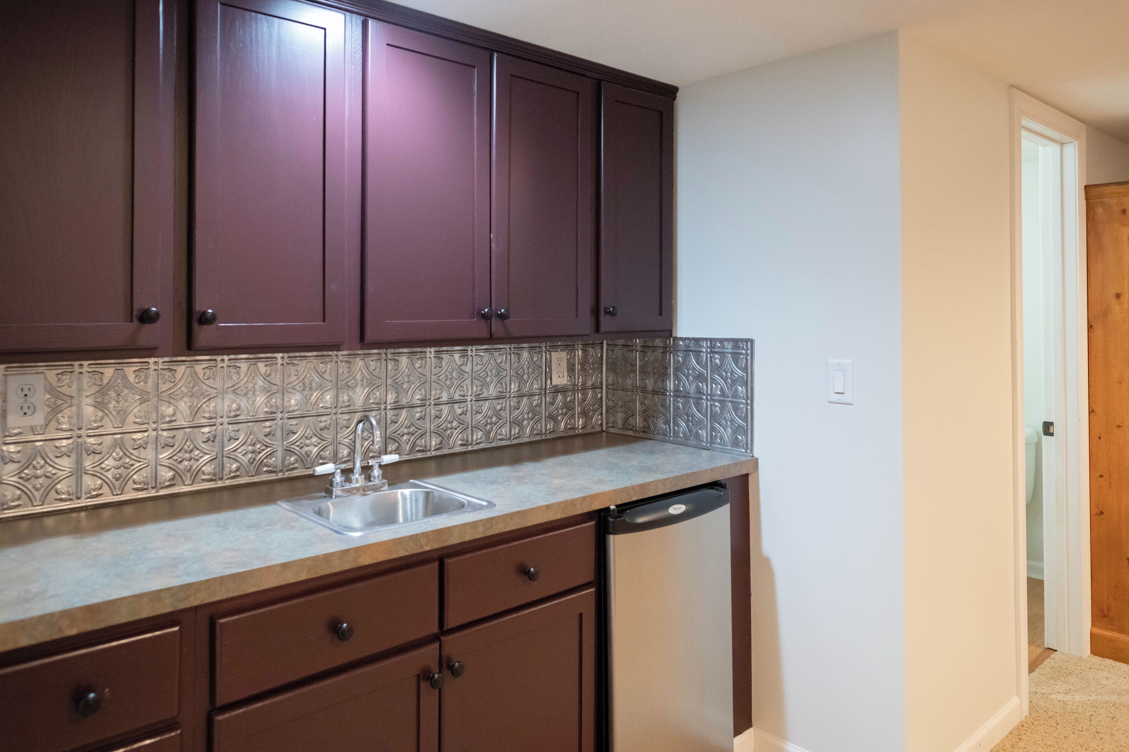 A kitchen with dark brown cabinets, a tiled backsplash, a stainless steel sink, and a dishwasher.